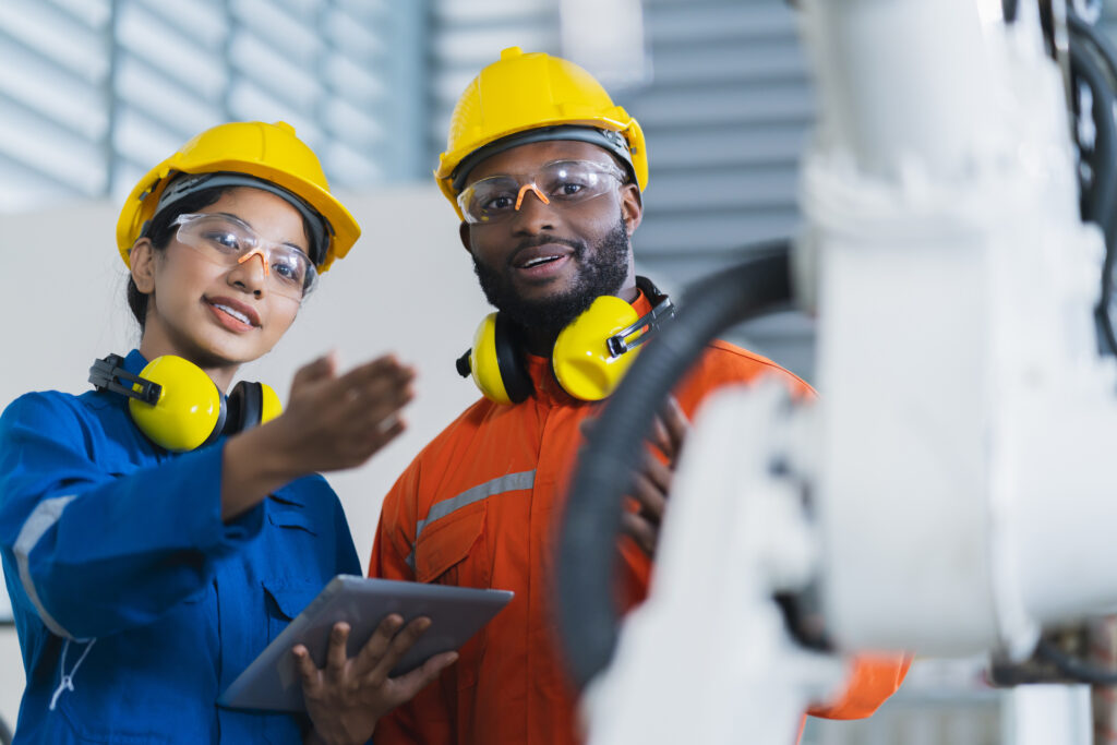 Two warehouse employees looking at machinery while holding a tablet