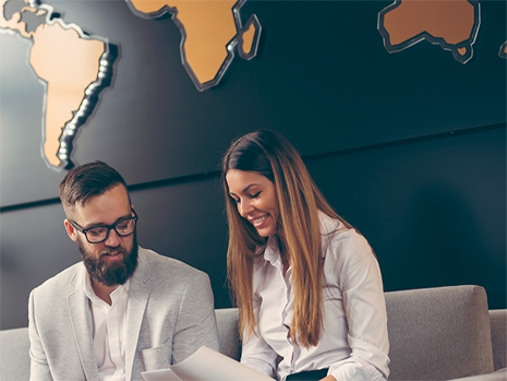 A man and a woman sitting on a couch in an office looking down at papers.