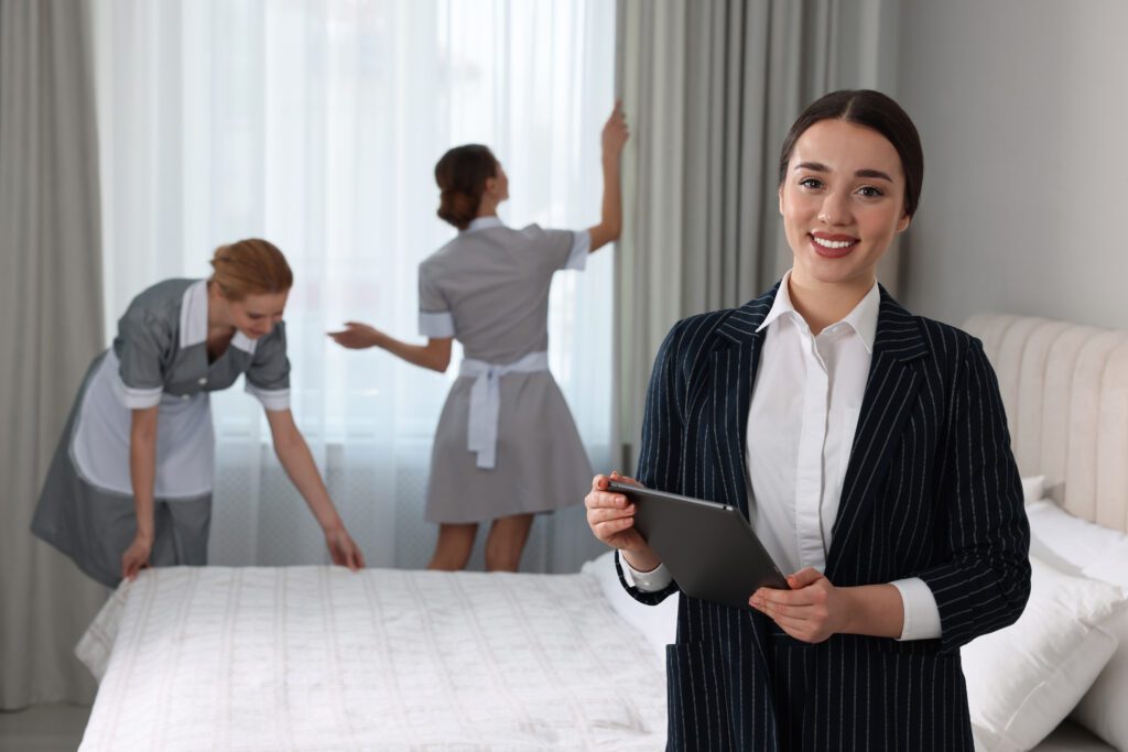 Housekeeping Manager With Tablet Checking Maid's Work In Hotel Bedroom.