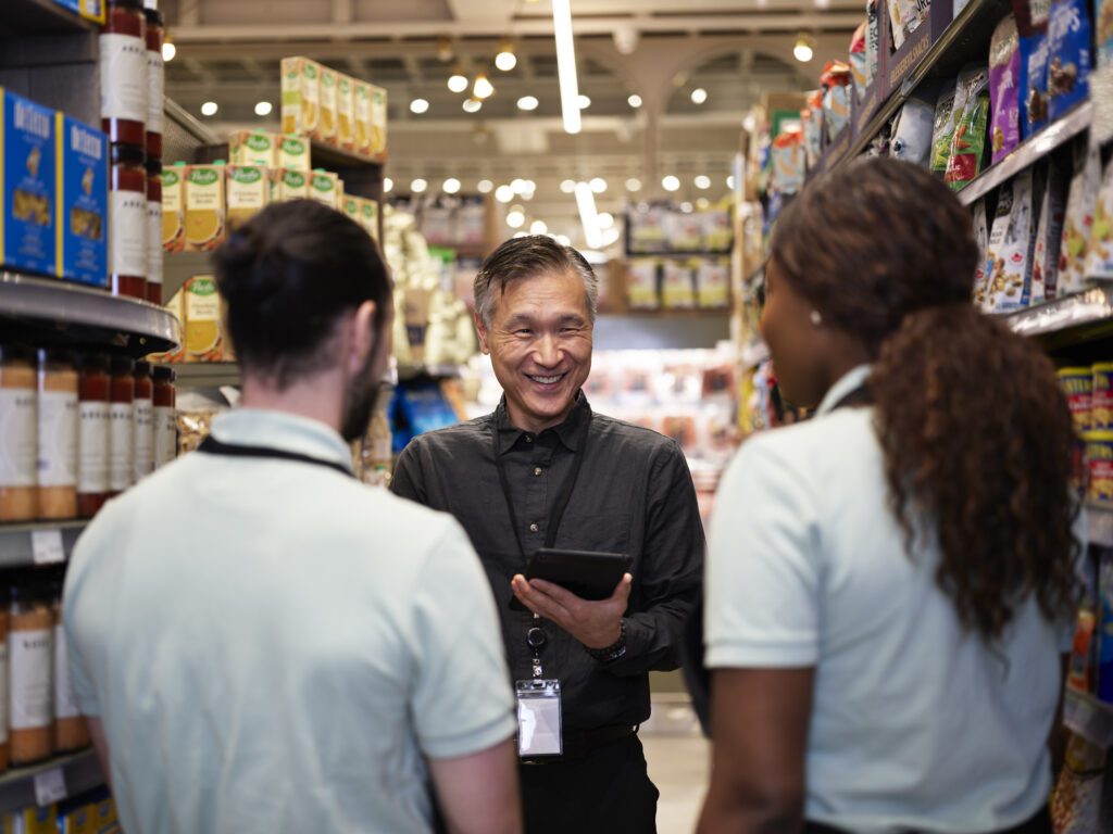Smiling grocery store manager providing meaningful employee rewards and recognition to 2 employees on the floor.
