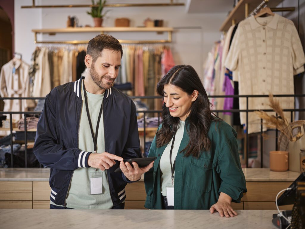 Two retail employees looking at task management on device in a clothing store.