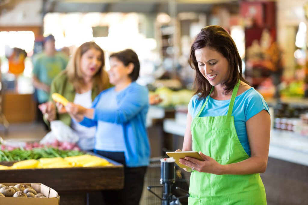 Grocery Store Employee Using Digital Tablet In Produce Section