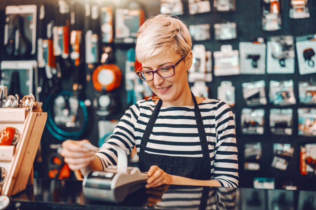 Female Worker Using Cash Register While Standing In Bicycle Store.