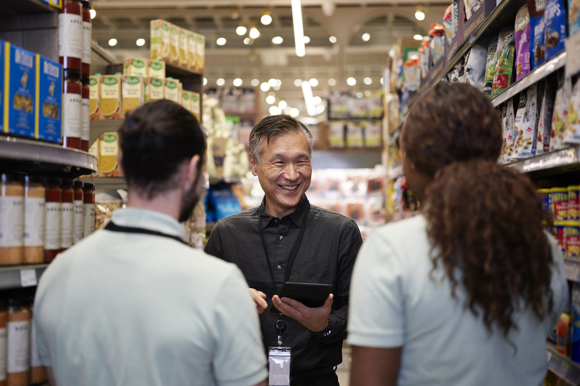 Manager holding tablet and smiling at 2 employees inside grocery store.